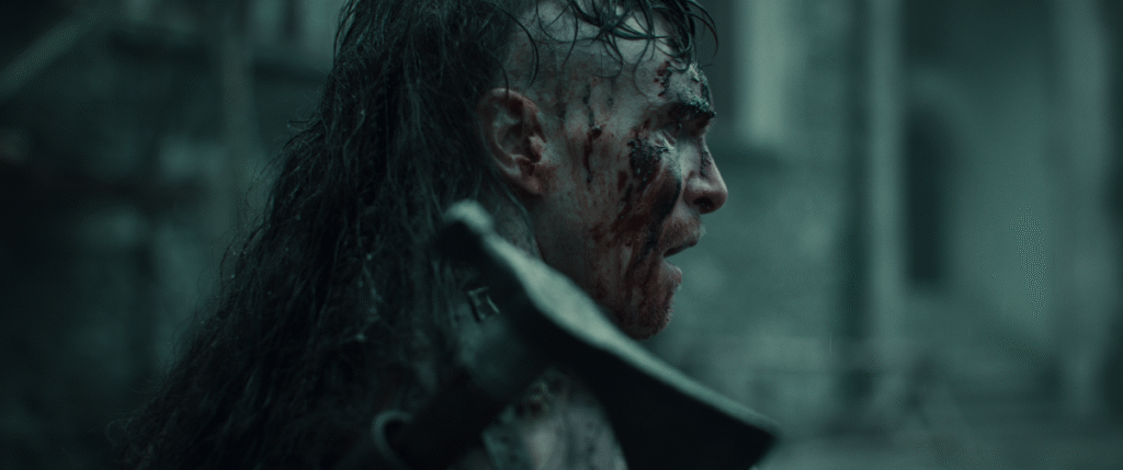Tomasz Włosok jako zakrwawiony, długowłosy wojownik w scenie walki z filmu "Dziki" Macieja Kawulskiego, ujęcie w wielkim formacie.