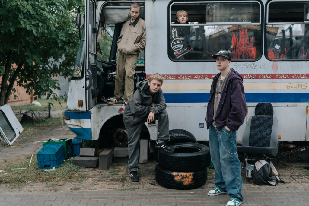 Młodzi bohaterowie pozują przy starym, zniszczonym autobusie. Kadr z filmu "Ministranci"