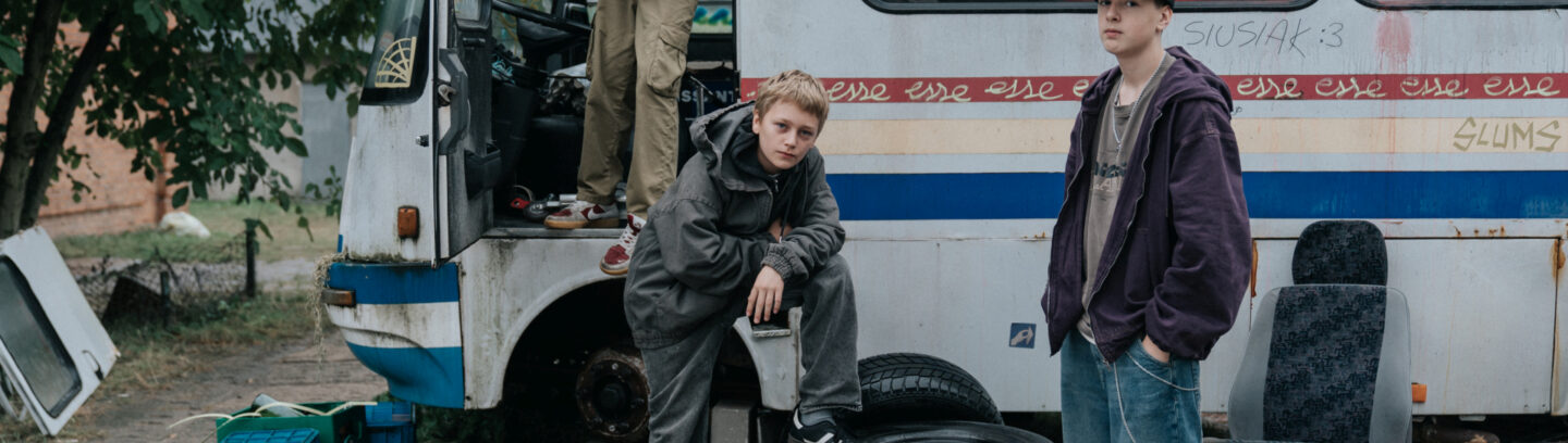 Młodzi bohaterowie pozują przy starym, zniszczonym autobusie. Kadr z filmu "Ministranci"