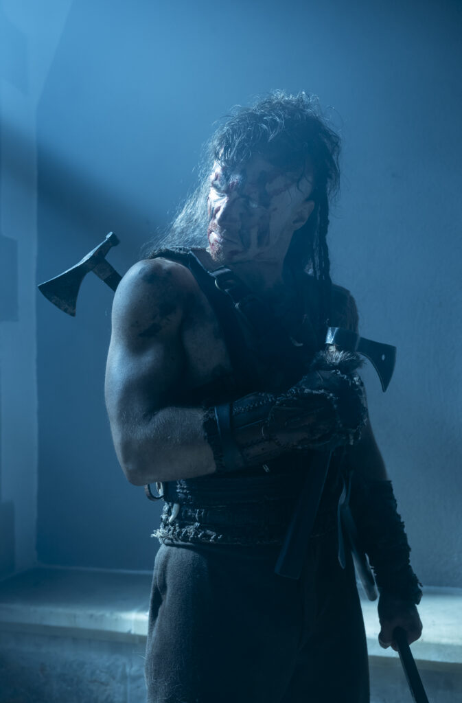 Postać wojownika (Tomasz Włosok) z dwoma toporami i krwią na twarzy w błękitnym świetle z filmu "Dziki" (reż. Maciej Kawulski).