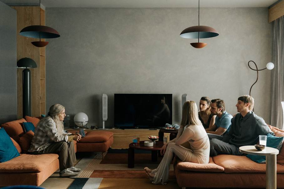 Starsza kobieta (Agata Kulesza) siedzi naprzeciw 4 młodych osób  (Michalina Łabacz, Dobromir Dymecki, Maciej Musiał,  Vanessa Aleksander) w nowoczesnym salonie z dużym telewizorem i niskimi stolikami; rozmieszczone na kanapach i fotelach w przestronnym, minimalistycznym wnętrzu.